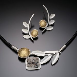 Handcrafted necklace with centerpiece of sterling silver leaf design next to bezel set dalmation jasper next to 22k gold dome in silver bezel suspended from a rubber cord for 18 inches total length