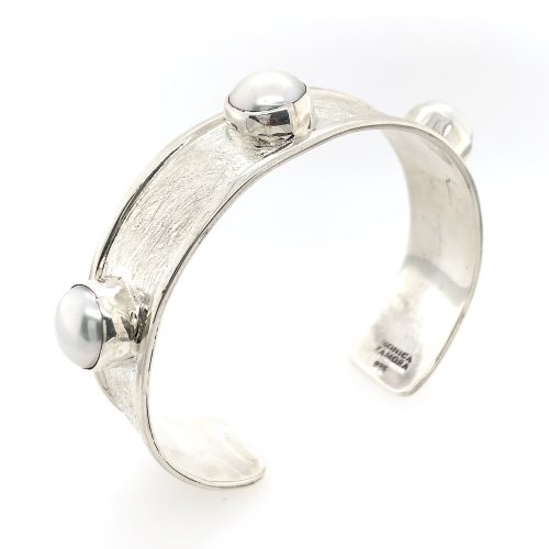 15mm sterling silver cuff bracelet, brushed finish with polished rim on both sides, has 3 10mm bezel set freshwater pearls evenly spaced across the top