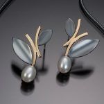 Oxidized sterling silver alternating leaf design post earrings with 18 k yellow gold stem structure leading to a white pearl bottom