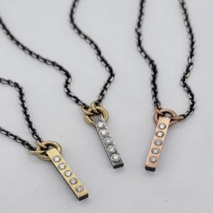 12MM VERTICAL OXIDIZED STERLING SILVER BAR SET WITH 0.12CT IN DIAMONDS WITH 18K YELLOW GOLD JUMP RING ON A 16” OXIDIZED STERLING SILVER CHAIN, PIC SHOWS THIS WITH A YELLOW GOLD VARIETY ON ITS LEFT AND A ROSE GOLD VARIETY ON ITS RIGHT